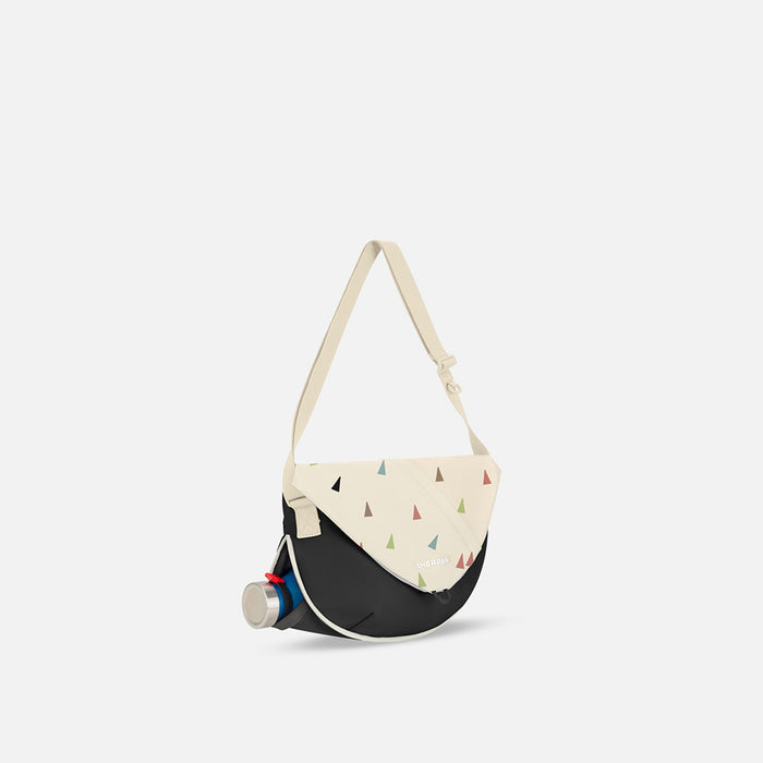 A Sherpani Milli Terrazzo Print Mini Messenger, 3/4 view showing front flap pocket and water bottle pocket on white backdrop. #color_terrazzo-print