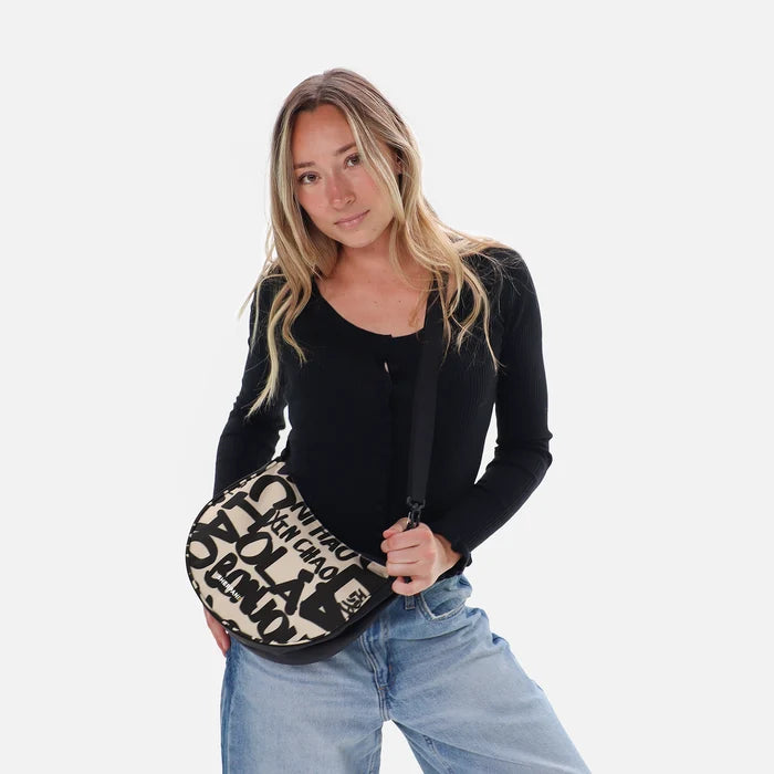 A woman holding a Sherpani Mina Ciao Medium Crossbody Bag in her hands with short-strap attachment. #color_ciao-print