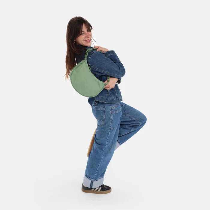 A woman wearing a Sherpani Mina Olivine Medium Crossbody Bag in her hands with short-strap attachment. #color_olivine-green