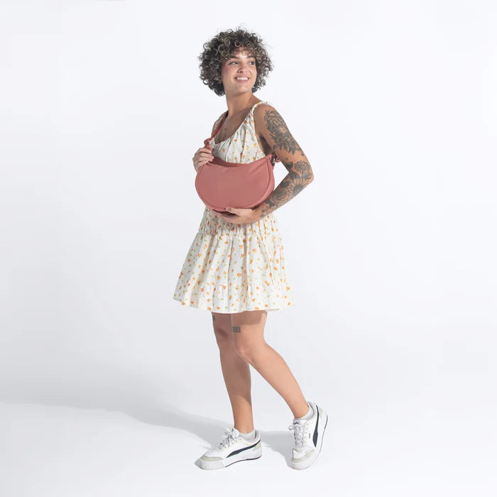 A woman holding a Sherpani Mina Desert Pink Medium Crossbody Bag in her hands with short-strap attachment. #color_desert-pink