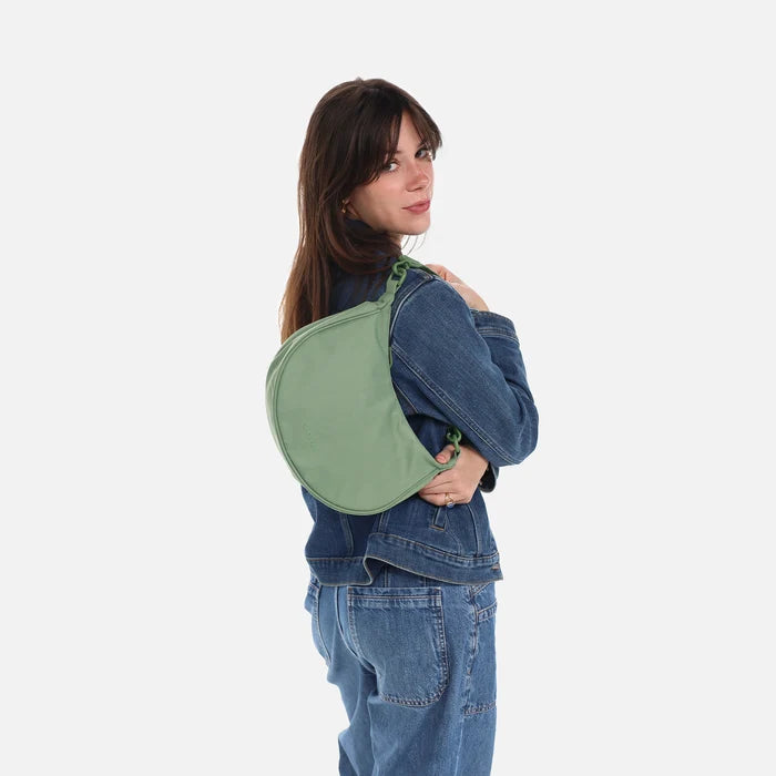 A woman wearing a Sherpani Mina Olivine Medium Crossbody Bag in her hands with short-strap attachment. #color_olivine-green