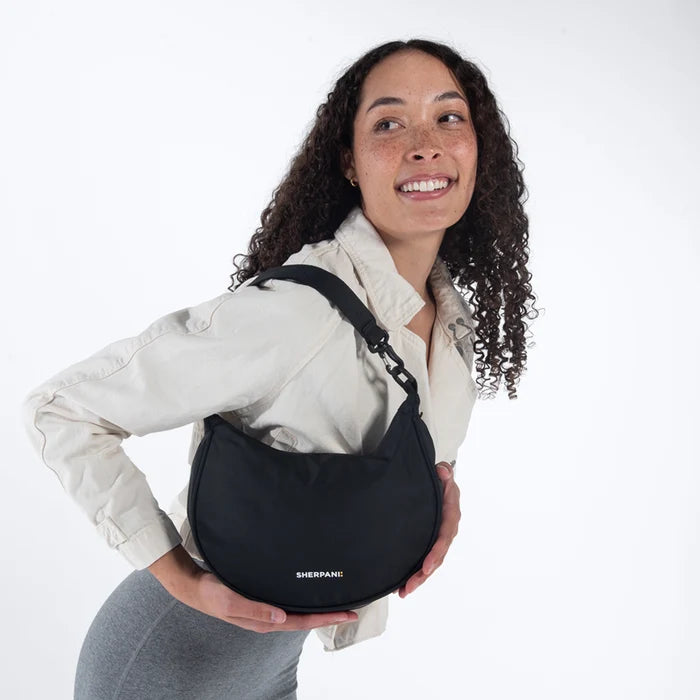 A woman holding a Sherpani Mina Raven Black Medium Crossbody Bag in her hands with short-strap attachment. #color_raven-black