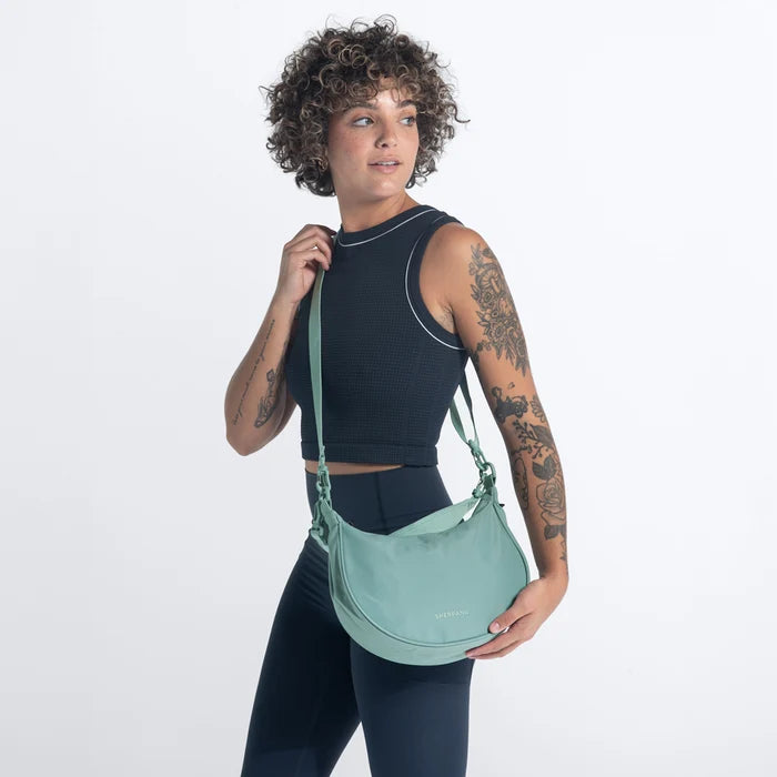 A woman holding a Sherpani Mina Surf Blue Medium Crossbody Bag in her hands with short-strap attachment. #color_surf-blue
