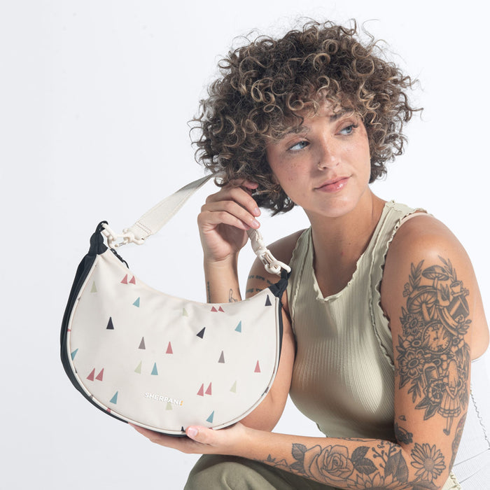 Woman holding a Sherpani Mina Terrazzo Print  Medium Crossbody Bag against white background.  #color_terrazzo-print