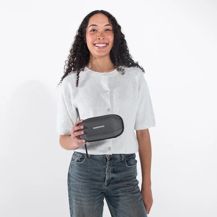 Woman holding a Sherpani Mini Co-Pilot Granite Mini Travel Organizer against white backdrop. #color_granite-grey