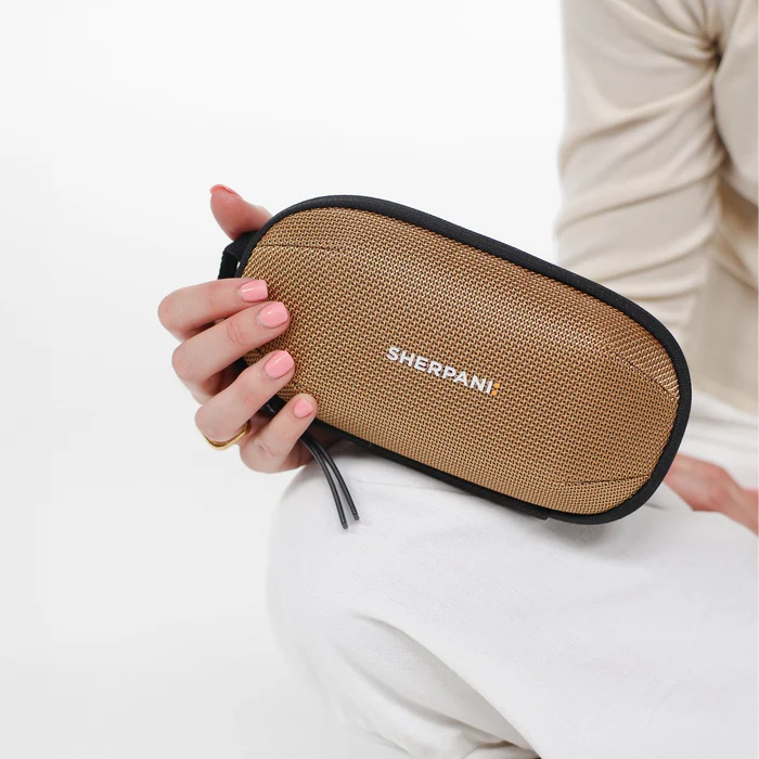Woman holding a Sherpani Mini Co-Pilot Sand Mini Travel Organizer against white backdrop. #color_sand-tan