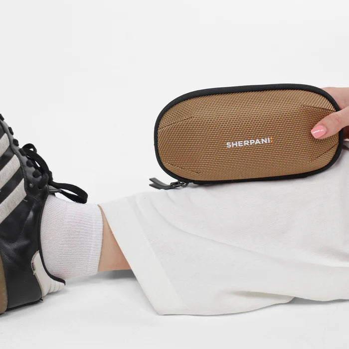 Woman holding a Sherpani Mini Co-Pilot Sand Mini Travel Organizer against white backdrop. #color_sand-tan