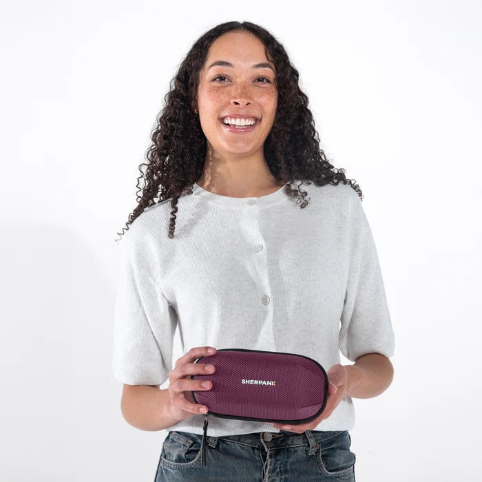 Woman holding a Sherpani Mini Co-Pilot Smoky Orchid Mini Travel Organizer against white backdrop. #color_smoky-orchid-pink