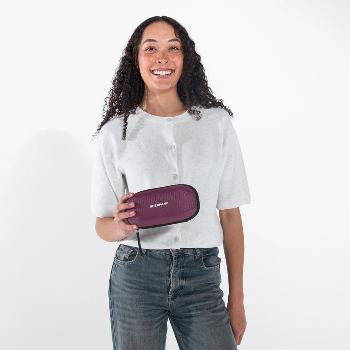 Woman holding a Sherpani Mini Co-Pilot Smoky Orchid  Mini Travel Organizer against white backdrop. #color_smoky-orchid-pink