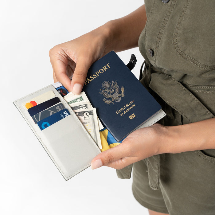 A person placing money into a Sherpani Osaka Moab Passport Holder against white background.  #color_moab