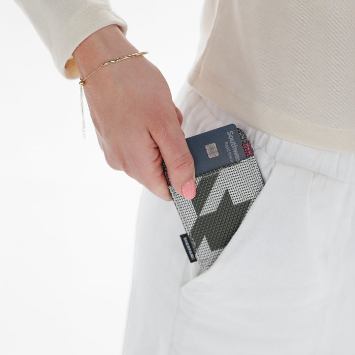 A woman placing a Sherpani Porter Houndstooth Credit Card Sleeve Wallet into her pant pocket against a white background. #color_houndstooth-print