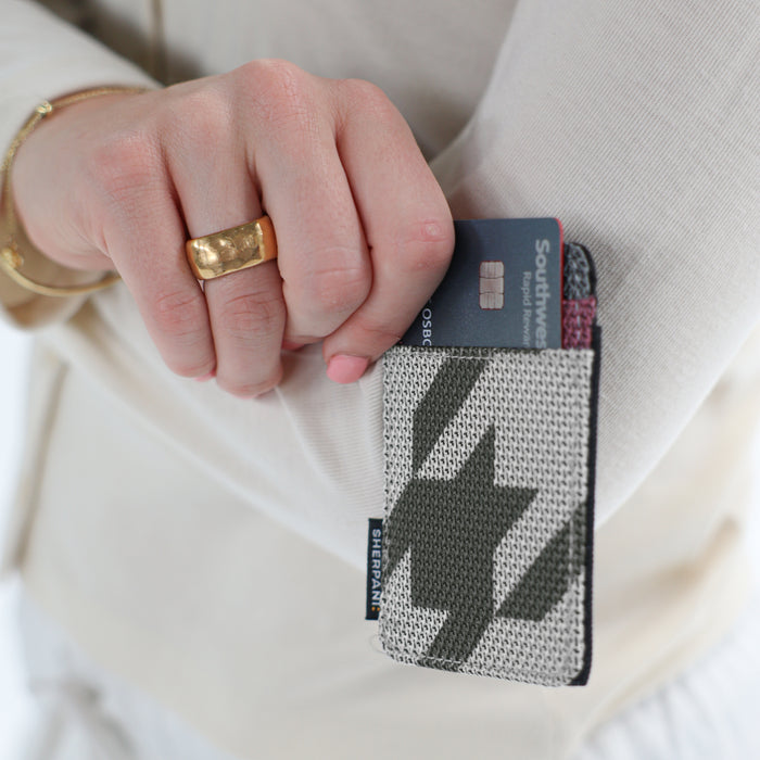 A woman holding a Sherpani Porter Houndstooth Credit Card Sleeve Wallet against a white background. #color_houndstooth-print