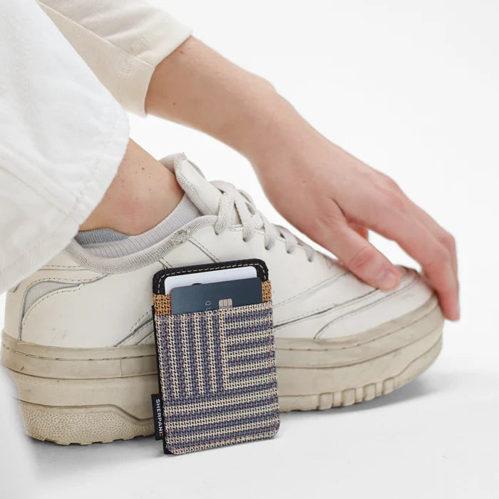 A woman sitting next to a Sherpani Porter Passport Credit Card Sleeve Wallet against a white background.  #color_passport-print