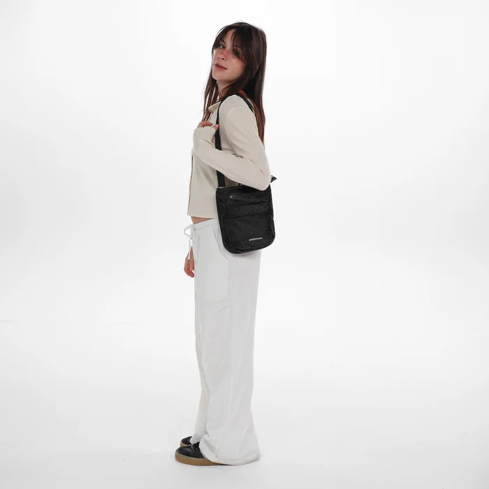 Woman wearing a Sherpani Prima Carbon Black Anti-Theft Travel Crossbody on her shoulder against white background. #color_carbon-black