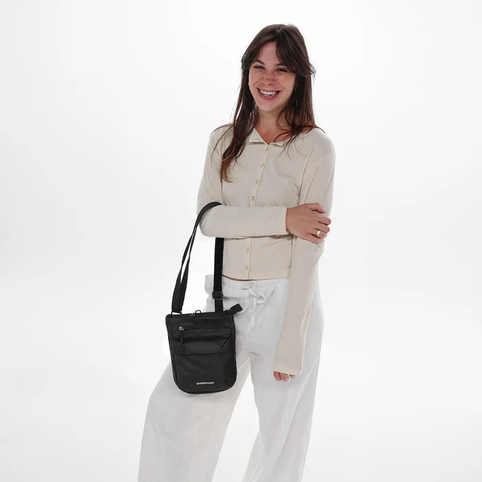 Woman holding a Sherpani Prima Carbon Black Anti-Theft Travel Crossbody by long strap against white background.  #color_carbon-black