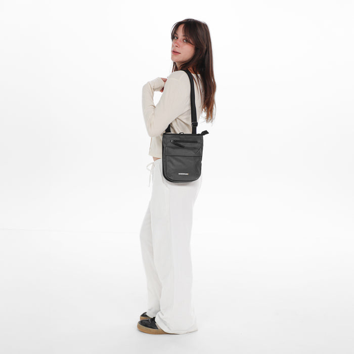 Woman wearing a Sherpani Prima Granite Anti-Theft Travel Crossbody on her shoulder against white background.  #color_granite-grey
