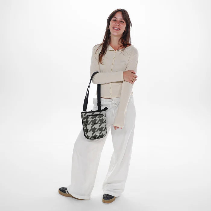 Woman holding a Sherpani Prima Houndstooth Anti-Theft Travel Crossbody by long strap against white background.  #color_houndstooth-print