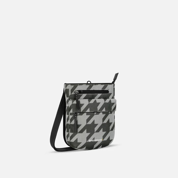 A Sherpani Prima Houndstooth Anti-theft Travel Crossbody, 3/4 view showing lockable pocket and strap on white background. #color_houndstooth-print
