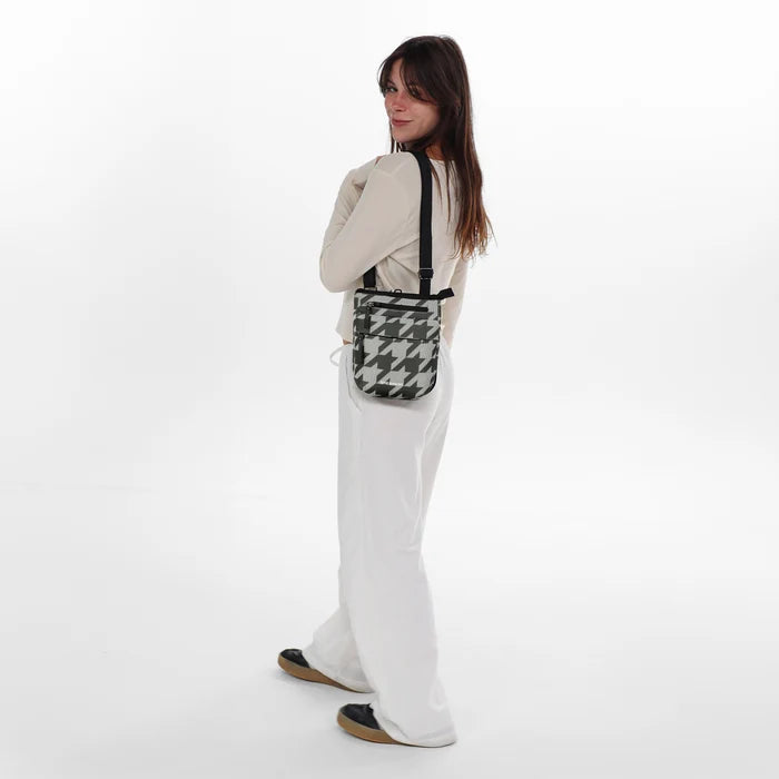 Woman wearing a Sherpani Prima Houndstooth Anti-Theft Travel Crossbody on her shoulder against white background.  #color_houndstooth-print
