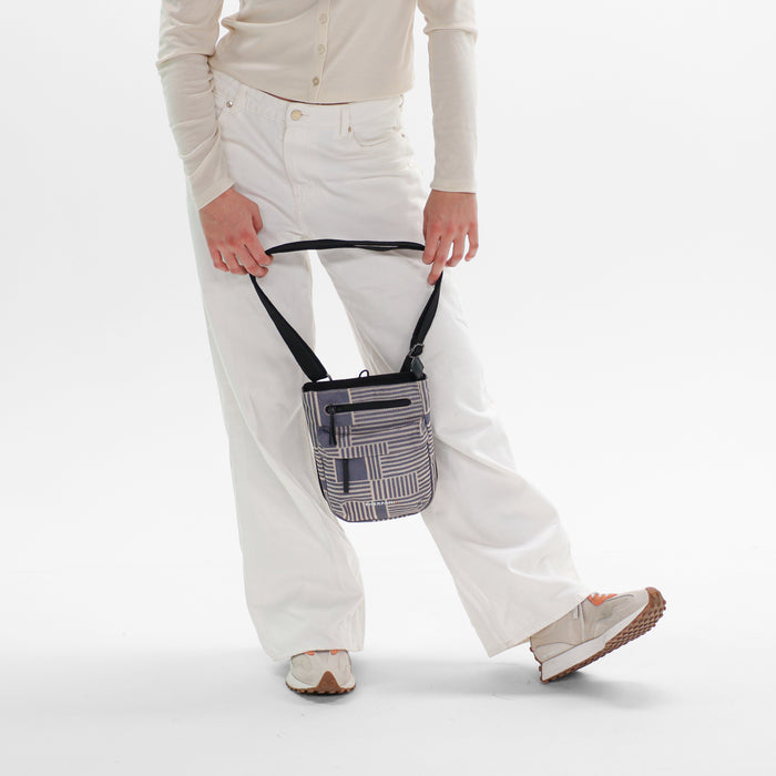 Woman holding a Sherpani Prima Passport Anti-Theft Travel Crossbody by long strap against white background.   #color_passport-print