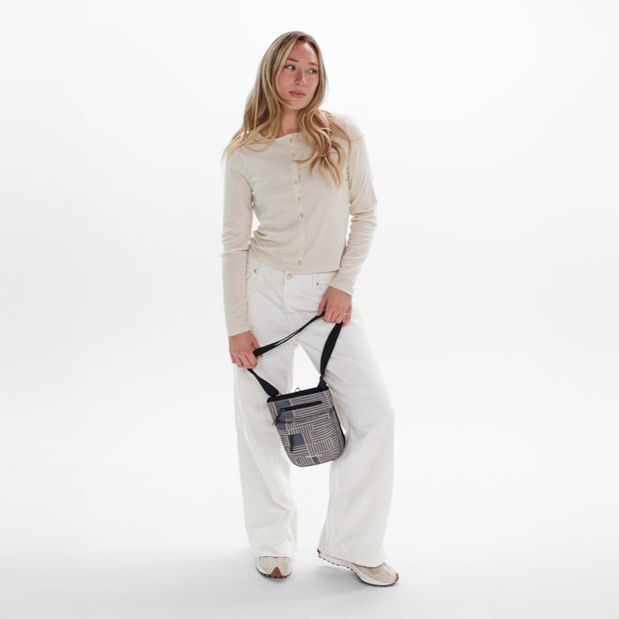 Woman holding a Sherpani Prima Passport Anti-Theft Travel Crossbody by long strap against white background.  #color_passport-print
