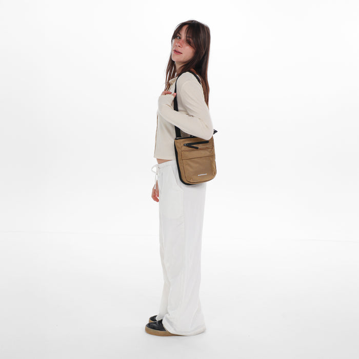 Woman wearing a Sherpani Prima Sand Anti-Theft Travel Crossbody on her shoulder against white background.  #color_sand-tan