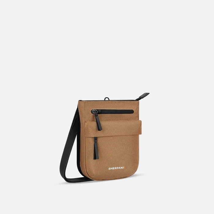 A Sherpani Prima Sand Anti-theft Travel Crossbody, 3/4 view showing lockable pocket and strap on white background. #color_sand-tan