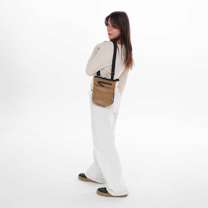 Woman wearing a Sherpani Prima Sand Anti-Theft Travel Crossbody on her shoulder against white background.  #color_sand-tan