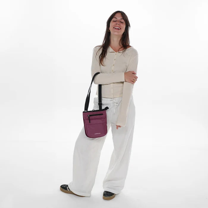 Woman holding a Sherpani Prima Smoky Orchid Anti-Theft Travel Crossbody by long strap against white background. #color_smoky-orchid-pink