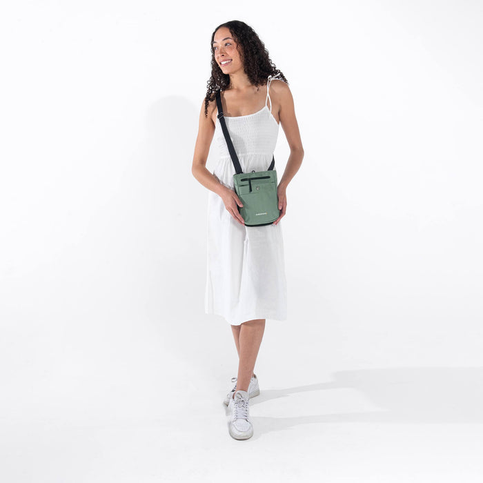 Woman wearing a Sherpani Prima Aloe Mist Green Travel Crossbody around her shoulder against white background.  #color_aloe-mist-green