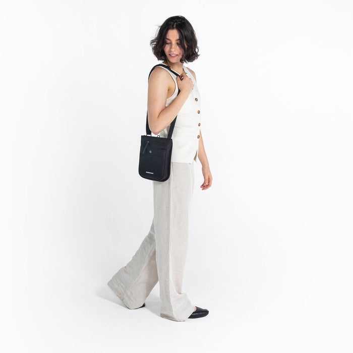 Woman wearing a Sherpani Prima Carbon Black Travel Crossbody on her shoulder against white background. #color_carbon-black