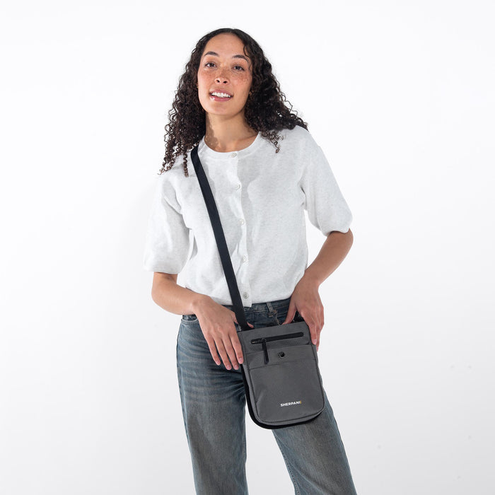 Woman wearing a Sherpani Prima Granite Travel Crossbody on her shoulder against white background.  #color_granite-grey