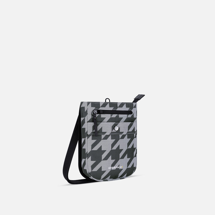 A Sherpani Prima Houndstooth Anti-theft Travel Crossbody, 3/4 view showing lockable pocket and strap on white background.  #color_houndstooth-print