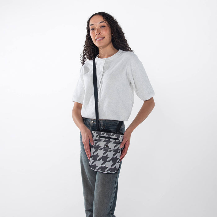 Woman wearing a Sherpani Prima  Houndstooth Travel Crossbody around her shoulder against white background. #color_houndstooth-print