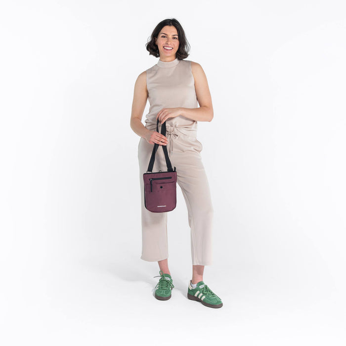 Woman holding a Sherpani Prima Smoky Orchid Travel Crossbody by adjustable strap against white background.  #color_smoky-orchid-pink