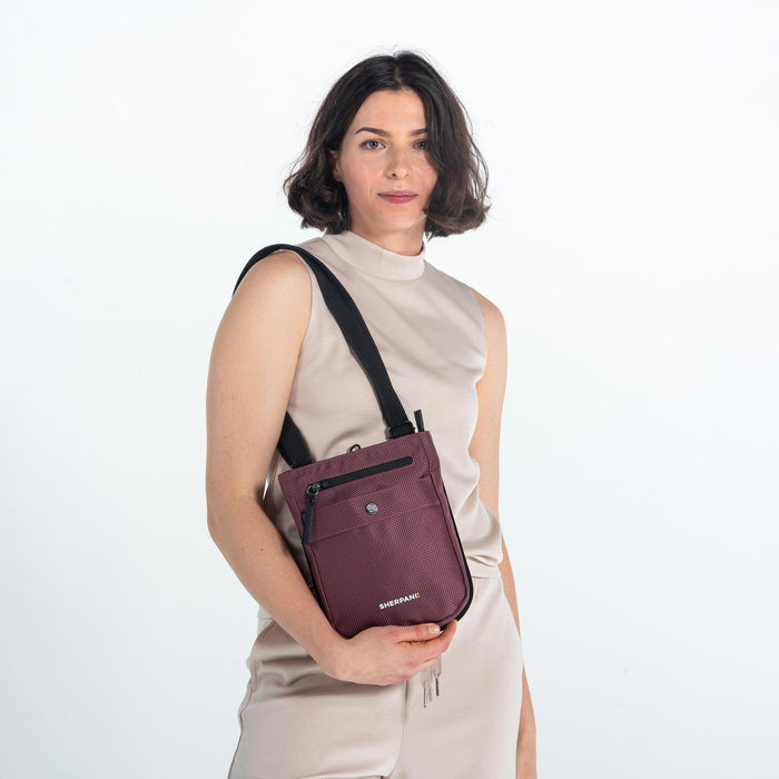 Woman wearing a Sherpani Prima Smoky Orchid Travel Crossbody on her shoulder against white background.  #color_smoky-orchid-pink