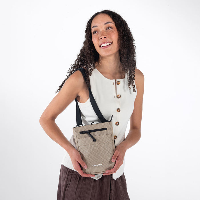 Woman wearing a Sherpani Prima Straw Beige Travel Crossbody on her shoulder against white background. #color_straw-beige