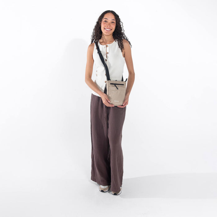 Woman wearing a Sherpani Prima Straw Beige Travel Crossbody on her shoulder against white background.  #color_straw-beige