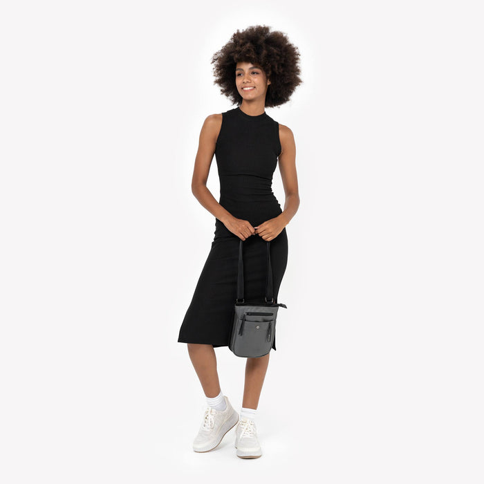 Woman holding a Sherpani Prima Granite Travel Crossbody by adjustable strap against white background. #color_granite
