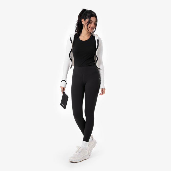 Woman holding a Sherpani Rio Black Passport Wallet by wrist strap on white backdrop. #color_black