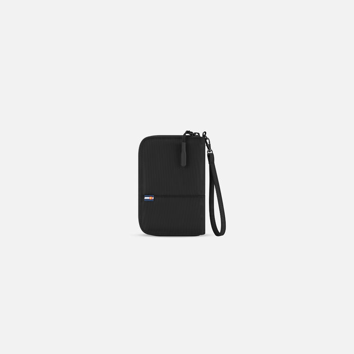 A Sherpani Rio Black Passport Wallet, back view showing wrist strap on white backdrop. #color_black