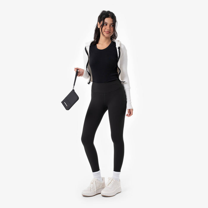 Woman holding a Sherpani Rio Black Passport Wallet by wrist strap on white backdrop. #color_black