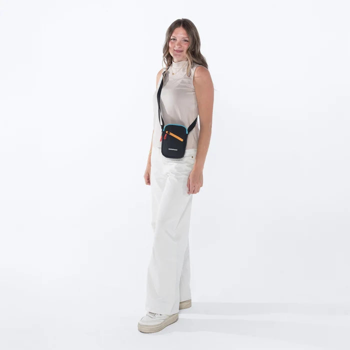 Woman wearing a Sherpani Rogue Chromatic Black Mini Crossbody on her shoulder against white background. #color_chromatic-black