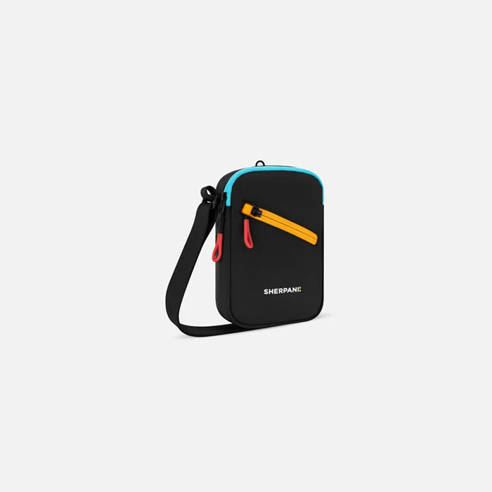 A Sherpani Rogue Chromatic Black Mini Crossbody, 3/4 view showing lockable pocket & strap on white backdrop.   #color_chromatic-black