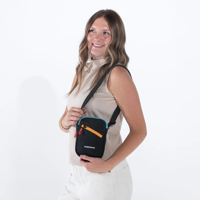 Woman wearing a Sherpani Rogue Chromatic Black Mini Crossbody on her shoulder against white background.   #color_chromatic-black