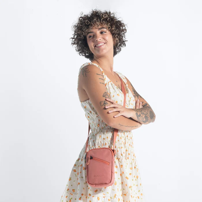 Woman wearing a Sherpani Rogue Desert Pink Mini Crossbody on her shoulder against white background.   #color_desert-pink