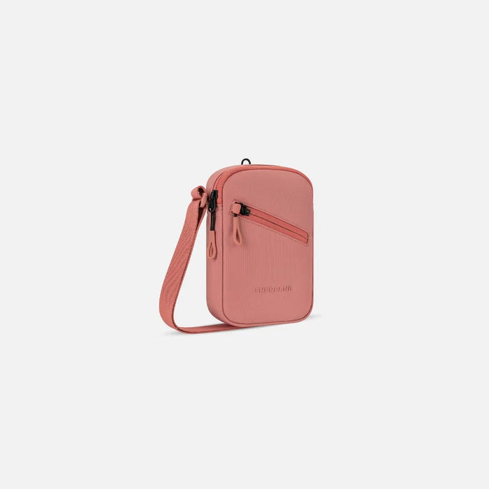 A Sherpani Rogue Desert Pink Mini Crossbody, 3/4 view showing lockable pocket & strap on white backdrop.   #color_desert-pink