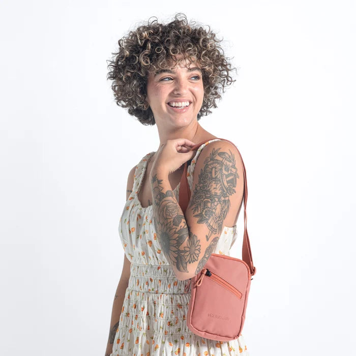 Woman wearing a Sherpani Rogue Desert Pink Mini Crossbody on her shoulder against white background.   #color_desert-pink