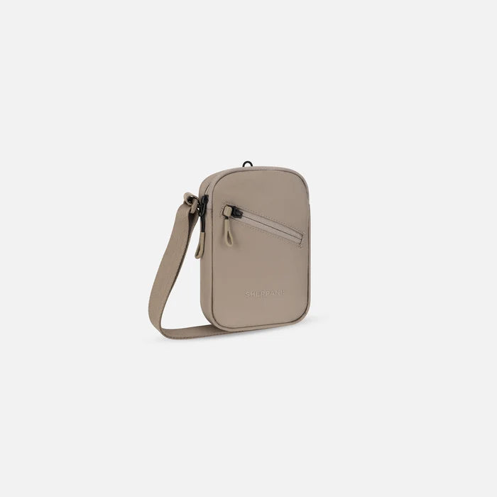 A Sherpani Rogue Dune Mini Crossbody, 3/4 view showing lockable pocket & strap on white backdrop. #color_dune-tan