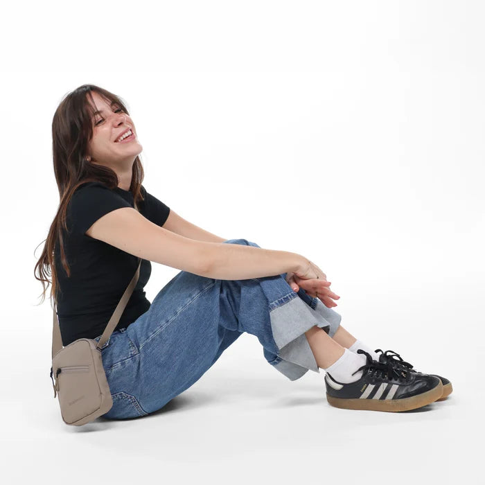 A woman sitting with a Sherpani Rogue Dune Mini Crossbody against white background.   #color_dune-tan